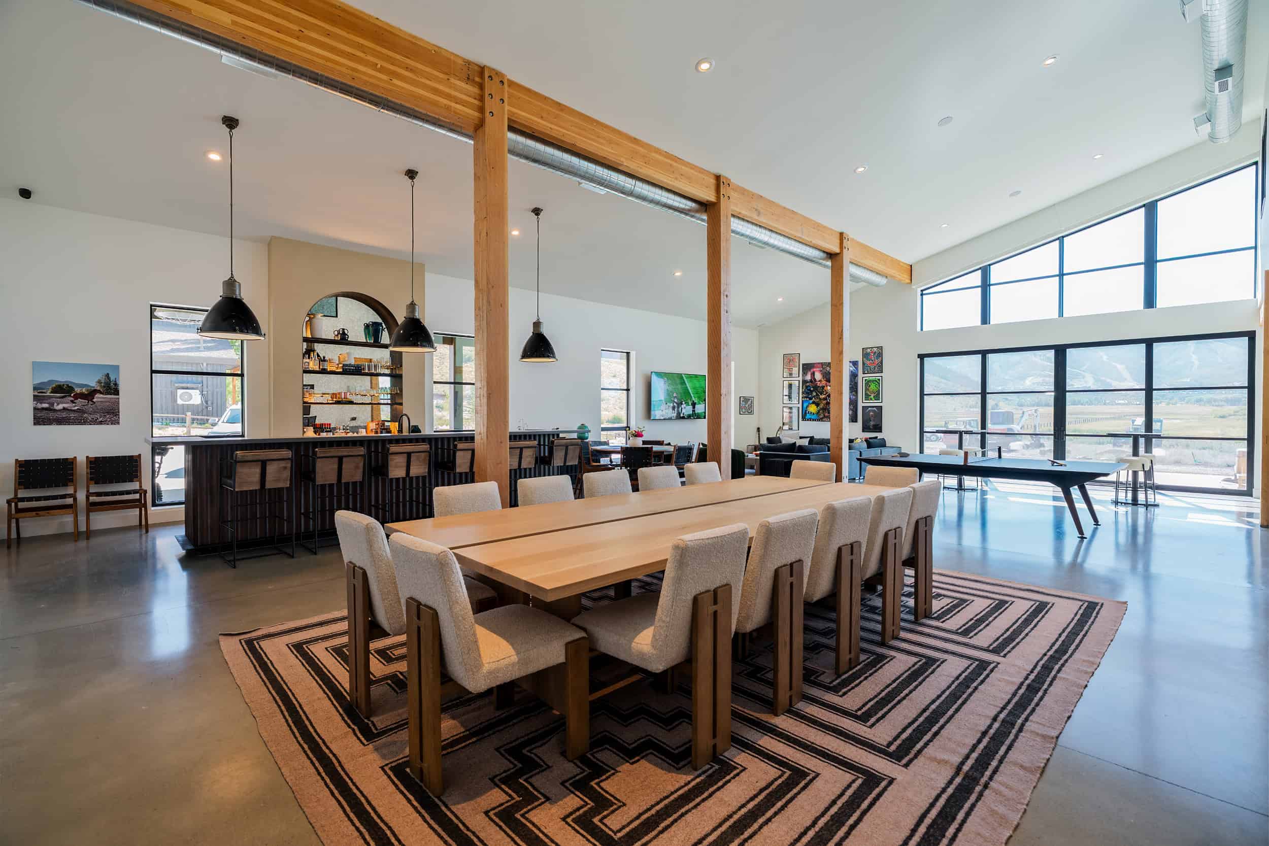 Bright modern game room featuring large windows, modern furniture, and a stylish bar in the background.