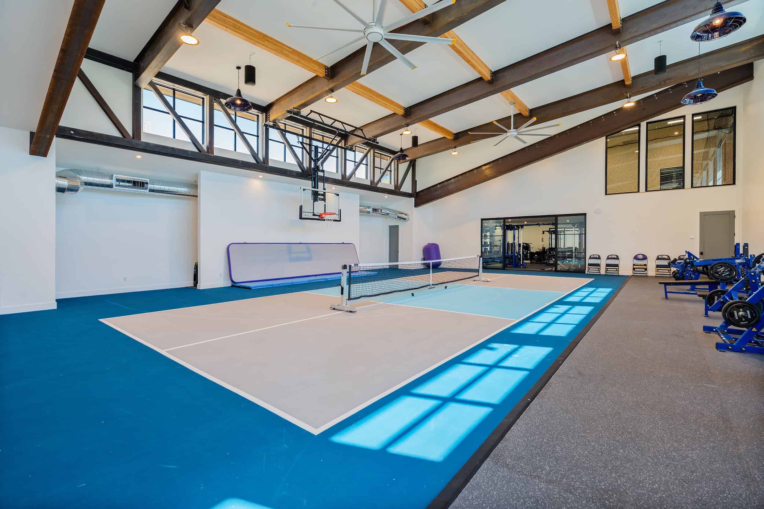 Bright luxury home sports gym with pickleball court, basketball hoop, and fitness gear with wide open space.
