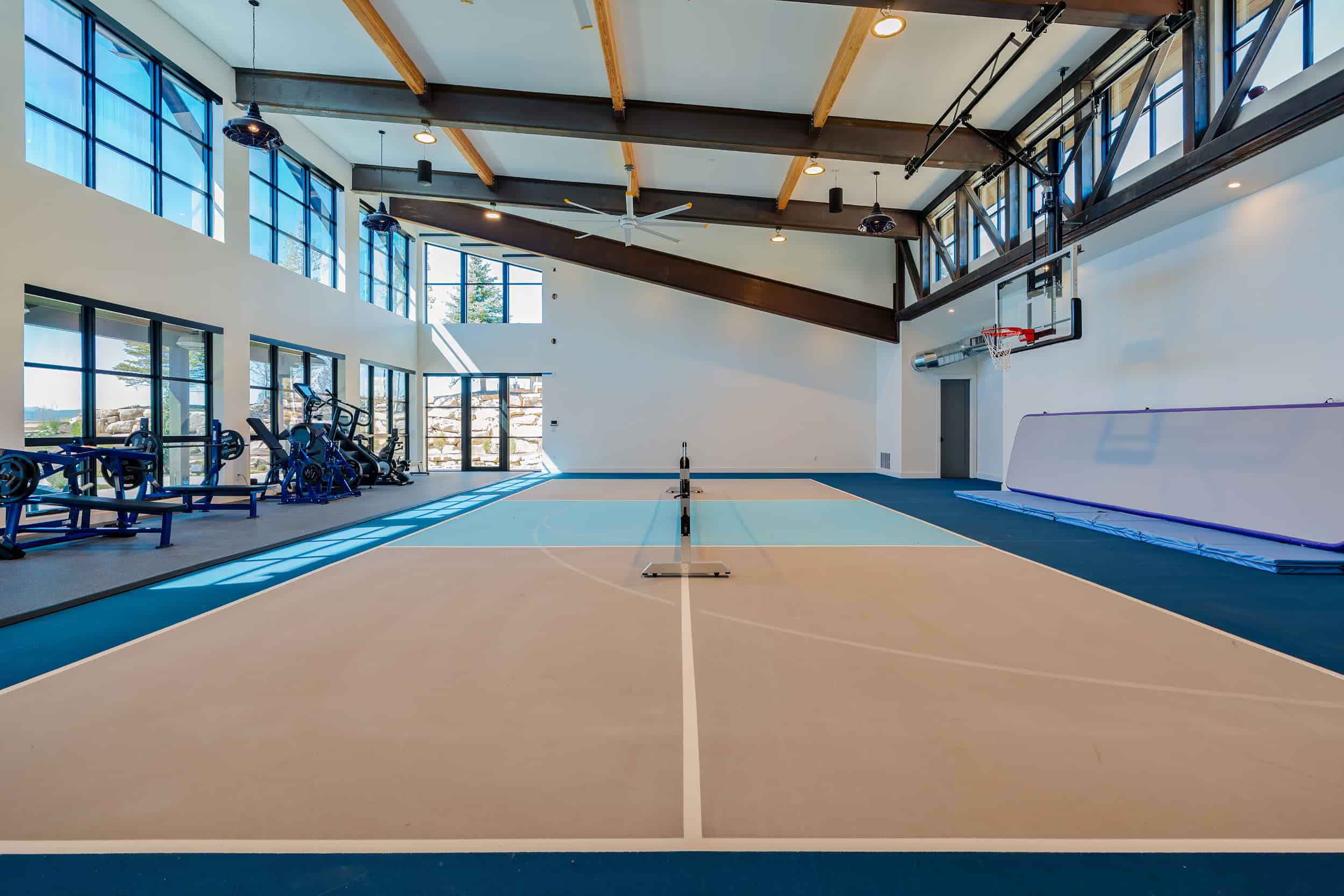 Bright indoor home gym featuring basketball hoop, workout machines, and large windows.