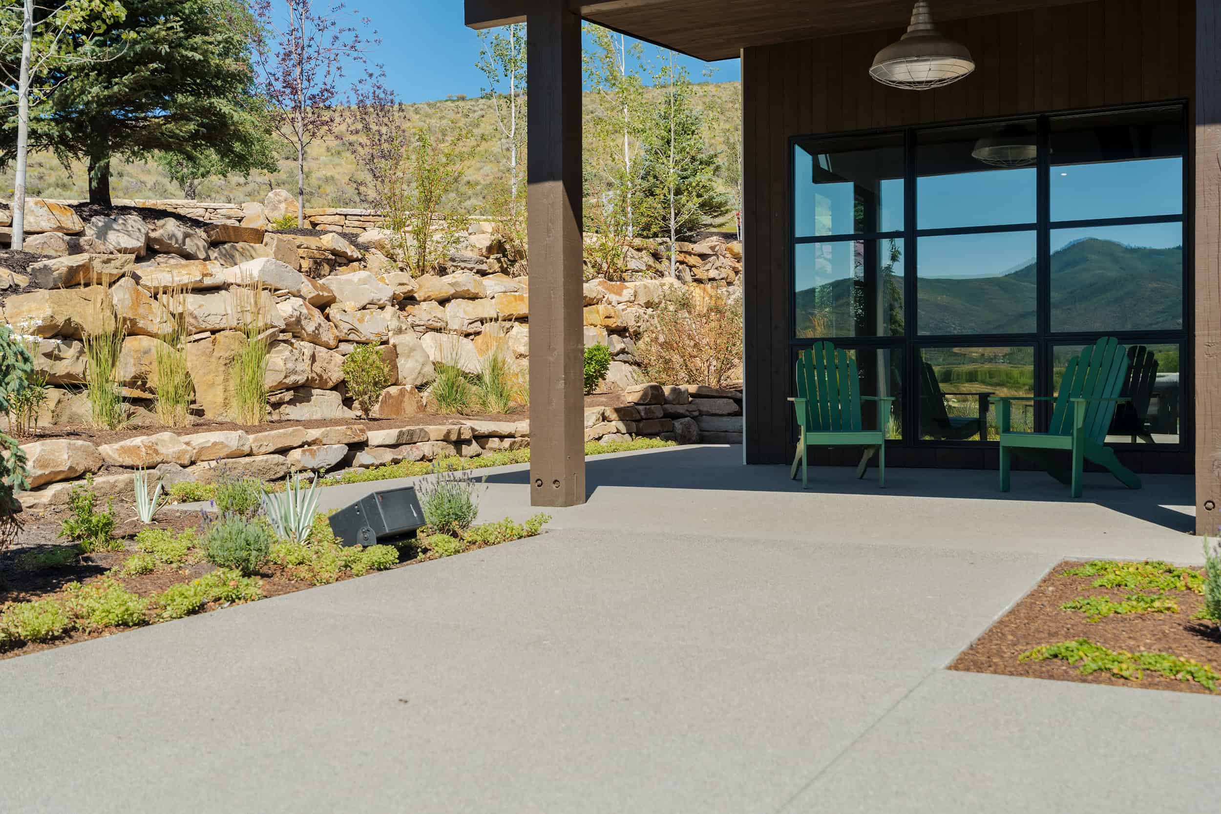 Outdoor patio with mountain view, rock landscaping, and green Adirondack chairs for relaxation.